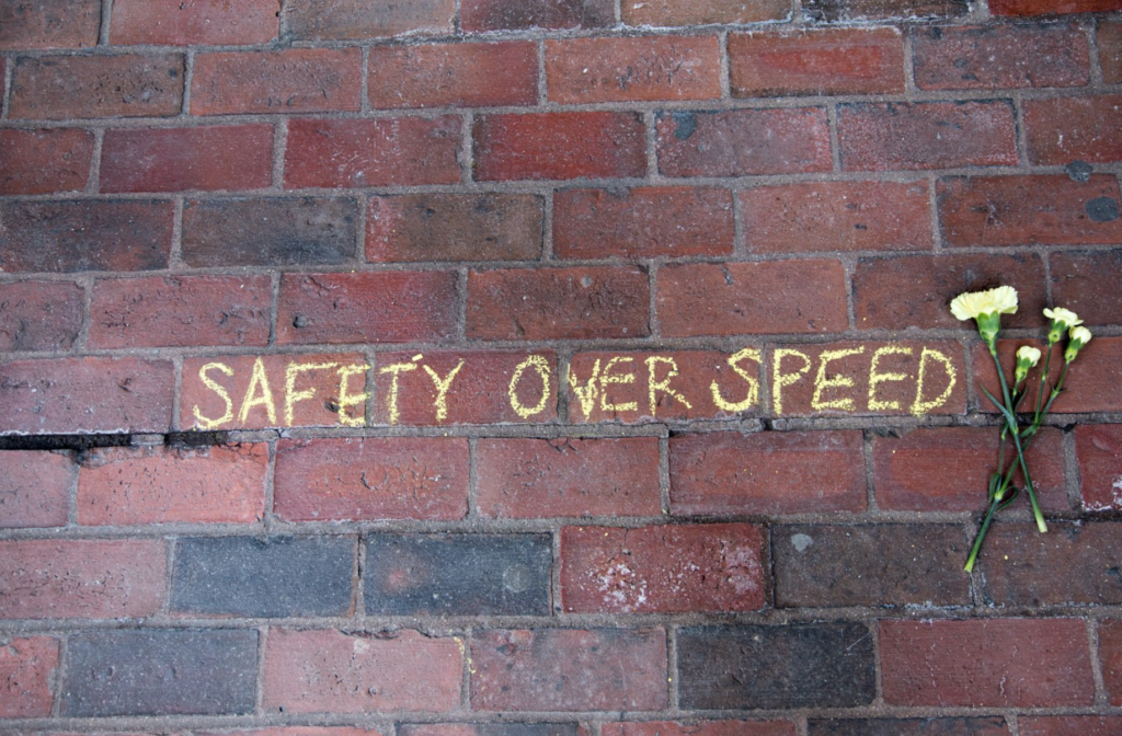 Overhead shot of brick road with "Safety over speed" written on it with chalk. White flowers are laid next to the writing.