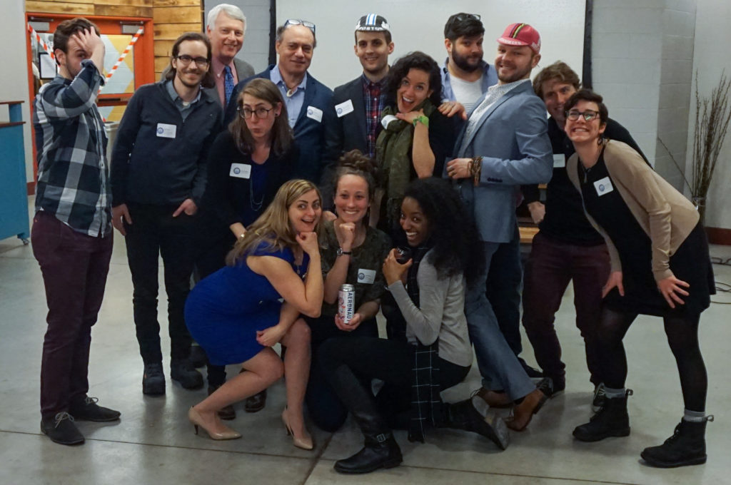 A group of people in semi-formal attire and nametags strike silly poses.