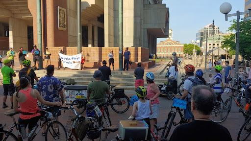 People with their bikes gathered at Boston City, On the steps, BCU organizers hold a sign that says, "People First Streets Now."