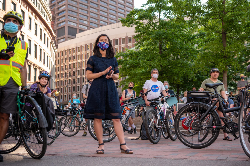 Mayor Michelle Wu claps her hands in City Hall Plaza, surrounded by people with bikes at a rally.