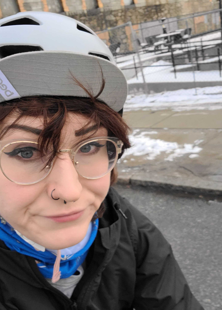 Mandy with their helmet and BCU buff on their bike, snow on the sidewalk is in the background