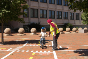 bike instructor helps a young child wearing a helmet practice biking skills on a "bike town" practice course 