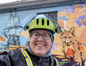 person wearing a yellow bike helmet smiling standing in front of a colorful mural